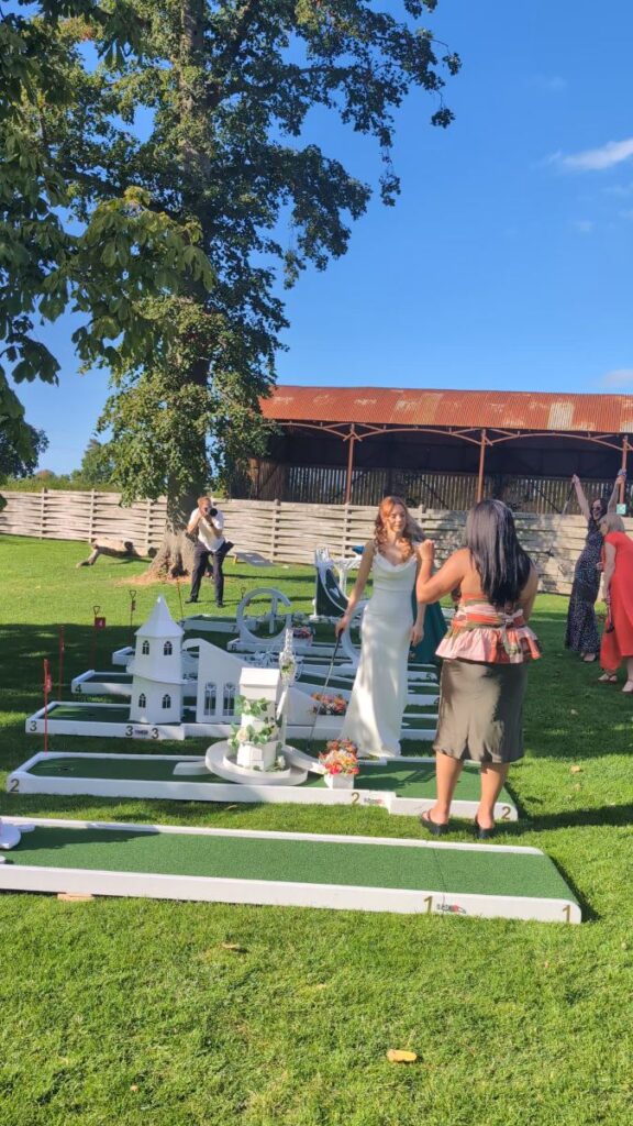 Wedding guests playing crazy golf on the lawn at Barns & Yard, with the barns behind