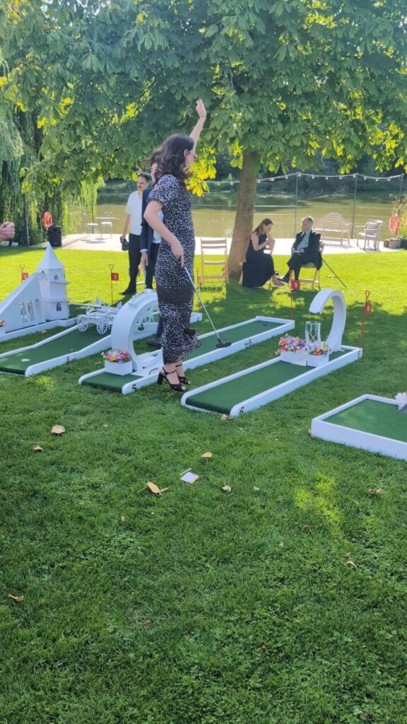 A guest celebrating on the wedding crazy golf course under the trees at Barns & Yard