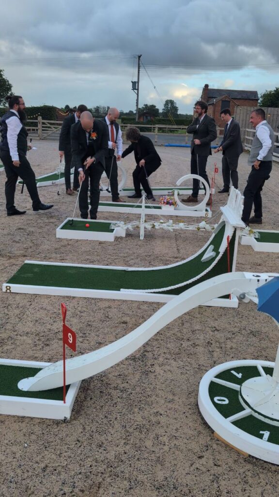 Guests playing wedding crazy golf on the arena at Burlton Manor, with the red-brick buildings behind