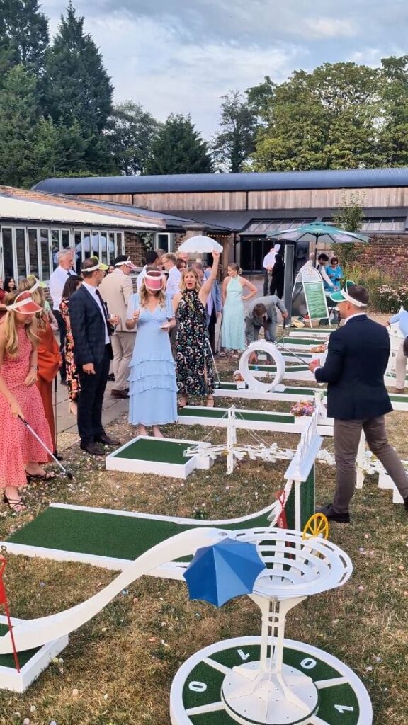 Wedding guests playing crazy golf in the walled garden at Foxtail Barns, with the Orangery behind